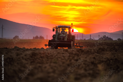 Beautiful sunset, farmer in tractor preparing land with seedbed cultivator © ValentinValkov