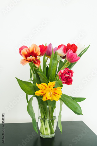 Bouquet of tulips in glass vase on black table. Beautiful spring flowers. White wall. Home decor.