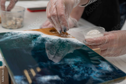 artist hands decorating a wooden serving board with white stones, epoxy resin, selective focus, imitation of the sea