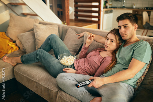 Relaxed couple watching TV and eating popcorn on the sofa at home.