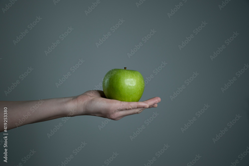 Woman`s hand holding green apple grey neutral background - raw photo. Dietary food and vitamins concept. Non-filtered template for product advertising. Woman`s hand holding green apple grey neutral background - raw photo. Dietary food and vitamins concept. Non-filtered template for product advertising.