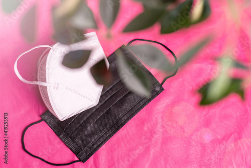 Face masks - a medical disposable black one and a white N95, NK95, FFP2. Bright pink background, plants in the foreground. Covid-19, Corona virus still-life. photo