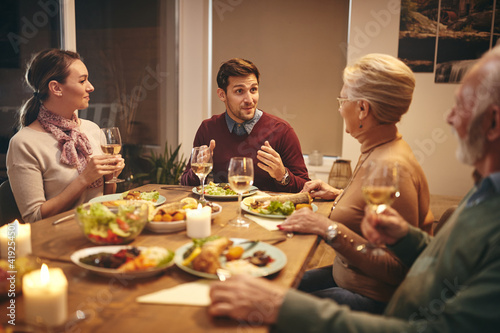 Young couple talking to senior couple during family dinner at dining table.
