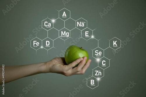 Woman`s hand holding green apple, microelement icons in molecular hexagons on grey background. Weight Loss concept template for product design. photo
