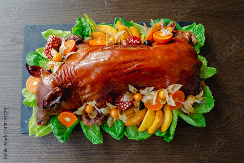 Restaurant menu. Baked suckling pig whole on a stone decorative board with fruit and physalis. Top view.