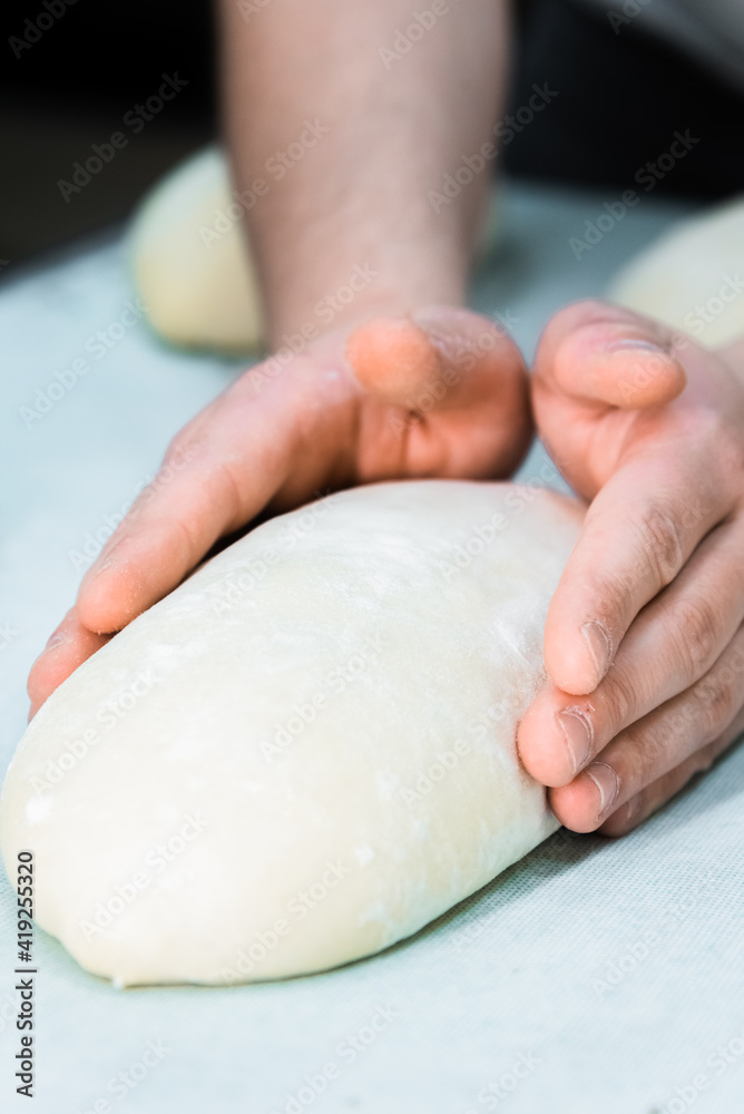 Baker making bread , man hands , kneading a dough , cooking coat.The concept of small bakeries, craft traditional bread Baker making bread , man hands , kneading a dough , cooking coat.The concept of small bakeries, craft traditional bread