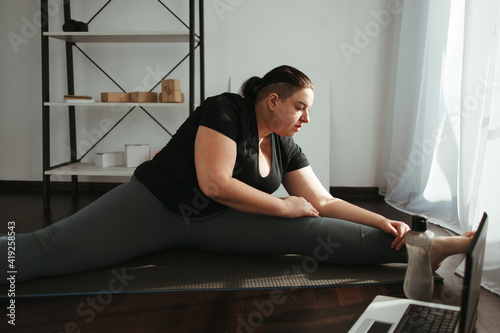 Home fitness, training online. Overweight woman looking tutorial video doing stretching exercise. Indoor yoga for home