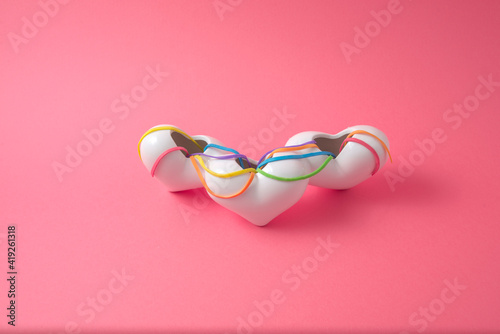 White hearts wrapped in multicolor bands with pink background.