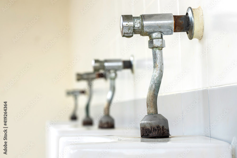 Rusty urinal faucets around an old urinal in the bathroom at the gas station. Dirty and unhygienic rust stains, space for text,Blurred background, Focus on the faucet.