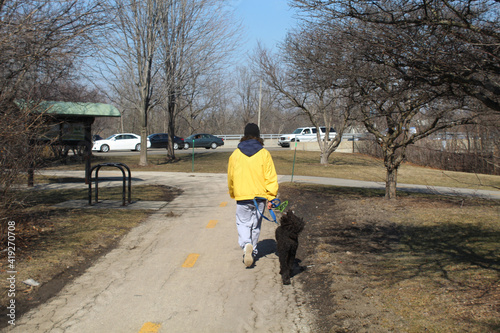 Man in a yellow coat walking his dog on a trail at the Skokie Northshore Sculpture Park in Skokie, Illinois