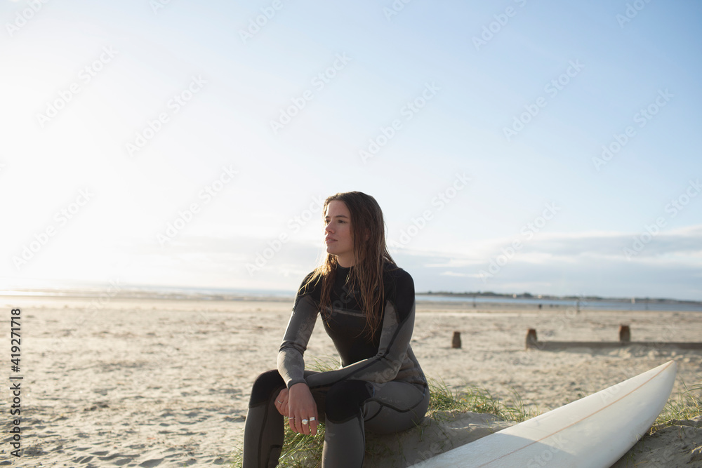 Serene beautiful young female surfer resting on sunny summer beach Serene beautiful young female surfer resting on sunny summer beach