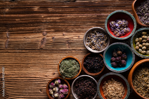 Natural medicine background. Assorted dry herbs in bowls and brass mortar on rustic wooden table.