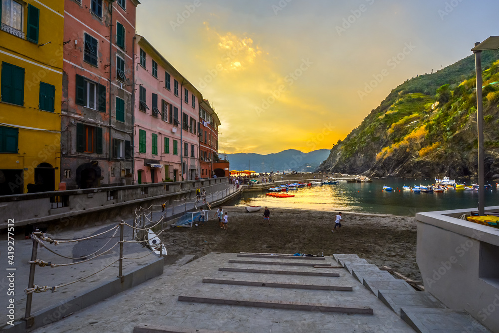 Obraz premium Children play along the sandy beach of Vernazza Italy harbor on the Cinque Terre as tourists enjoy a sunset dinner along the pier.