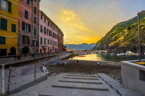 Children play along the sandy beach of Vernazza Italy harbor on the Cinque Terre as tourists enjoy a sunset dinner along the pier.