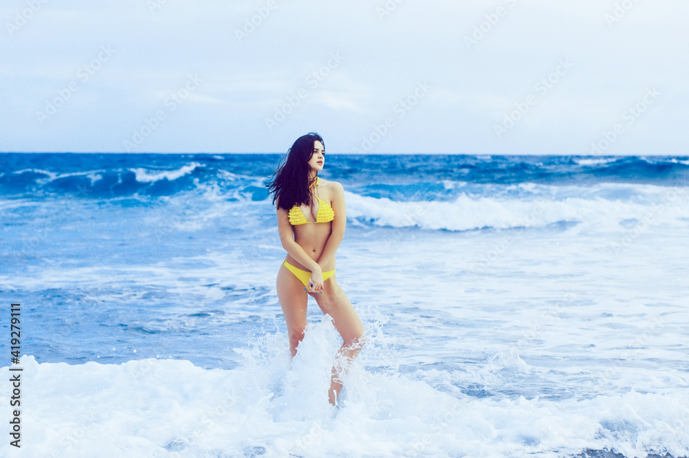 Young woman in swimsuit in white sea foam on summer day.