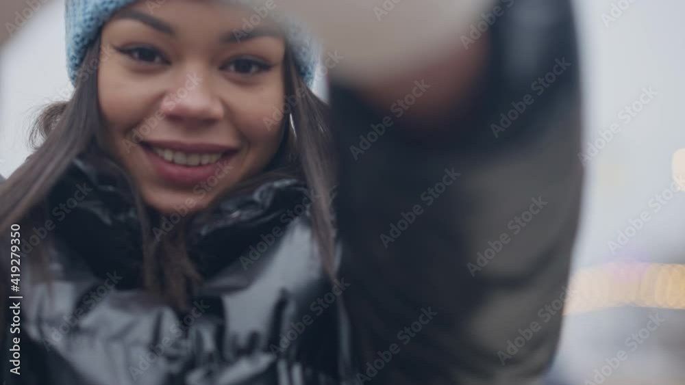 Cheerful young millennial woman hiding face with hand in white mittens on misty winter day. Portrait of joyful African American lady having fun resting on New Year's eve outdoors. Cheerful young millennial woman hiding face with hand in white mittens on misty winter day. Portrait of joyful African American lady having fun resting on New Year's eve outdoors.
