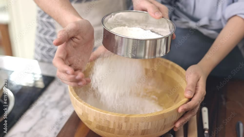 Asian couple Help each other to make a bakery In a romantic atmosphere in the kitchen at home. Young people work together to mix the ingredients in a wooden bowl before stirring them together. Asian couple Help each other to make a bakery In a romantic atmosphere in the kitchen at home. Young people work together to mix the ingredients in a wooden bowl before stirring them together.