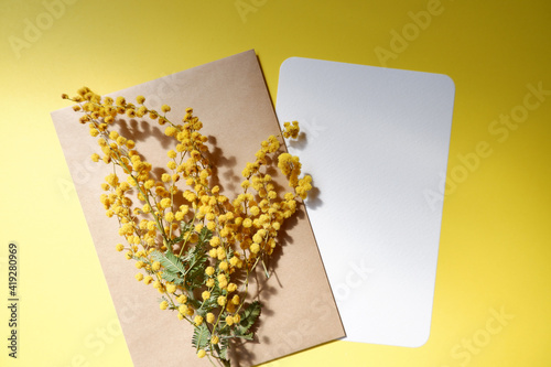 Spring greeting concept. Mimosa flowers decoration with a blank greeting card on yellow background. Spring background elements.　黄色背景にカードとミモザの花、春の挨拶、メッセージカードとミモザ