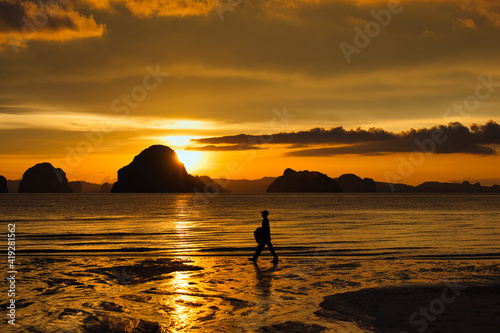 Fototapeta Naklejka Na Ścianę i Meble -  Male fisherman silhouette walking by the sea at sunset, golden hour background is island and mountain, warm tone, Andaman sea beach in Krabi, Thailand.