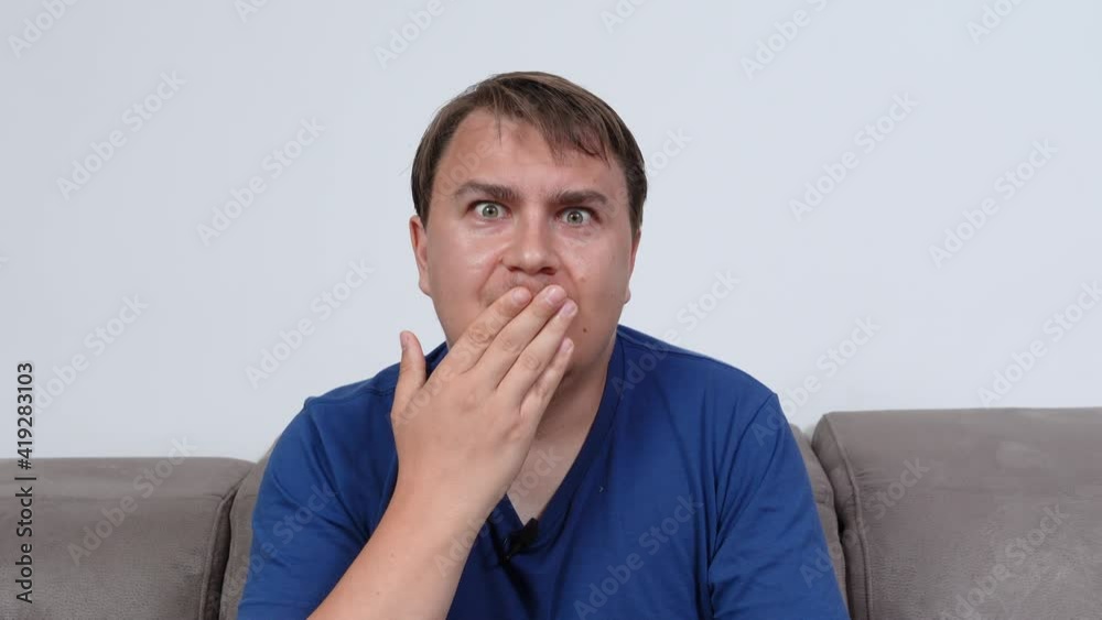 Funny wondered young man with microphone fixed on blue clothes shoots video sitting on comfortable couch in living room closeup Funny wondered young man with microphone fixed on blue clothes shoots video sitting on comfortable couch in living room closeup