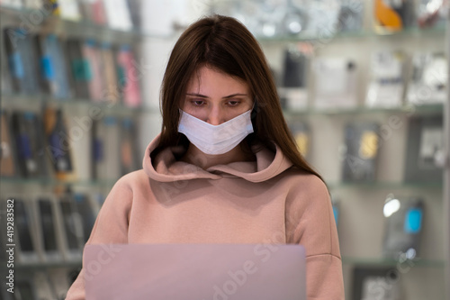 Woman in a mask working in a shop with laptop.