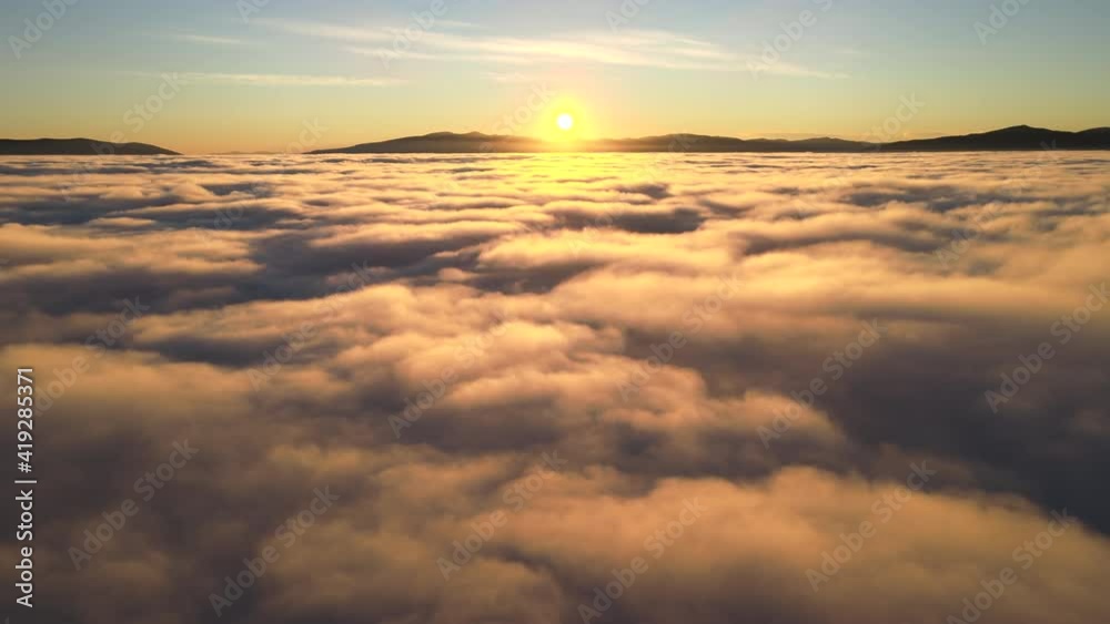 Aerial view of vibrant yellow sunrise over white dense clouds and distant mountains on horizon. Aerial view of vibrant yellow sunrise over white dense clouds and distant mountains on horizon.