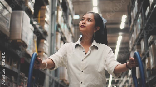 Asian woman with shopping cart walking for choosing new furniture in big store warehouse.