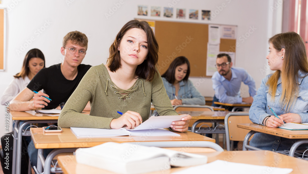 Fototapeta premium Young girl is writing test and thinking about questions at the desk in the class.