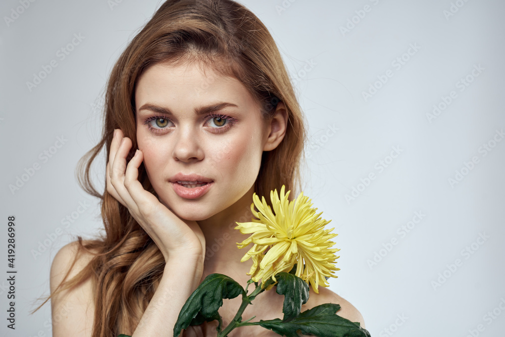 Portrait of a beautiful woman with a yellow flower on a light background cropped with Copy Space Model