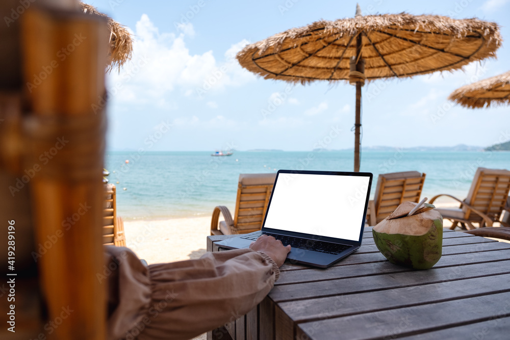 Mockup image of a woman using and touching on laptop touchpad with blank desktop screen while sitting on the beach