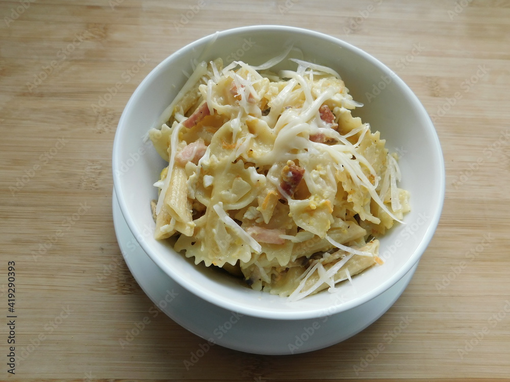 pasta farfalle with mushrooms, cheese and bacon in a white plate on a wooden table. pasta farfalle with mushrooms, cheese and bacon in a white plate on a wooden table.
