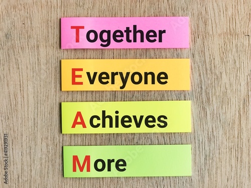 Team concept.Phrase TOGETHER EVERYONE ACHIEVES MORE written on colorful sticky note isolated on wooden background.