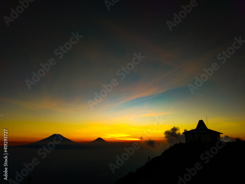  The view of the twilight from the top of the mountain with an orange sky and a tomb building on the mountain