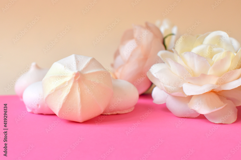 Festive postcard. Small meringue  and flowers on pink background. Space for text. Background in pastel colors with sweets and flowers. Selecktive focus