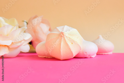 Festive postcard. Small meringue and flowers on pink background. Space for text. Background in pastel colors with sweets and flowers. Selecktive focus
