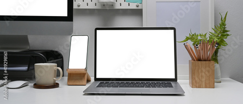 Horizontal image of modern workplace with smart phone, laptop and computer pc on white table.