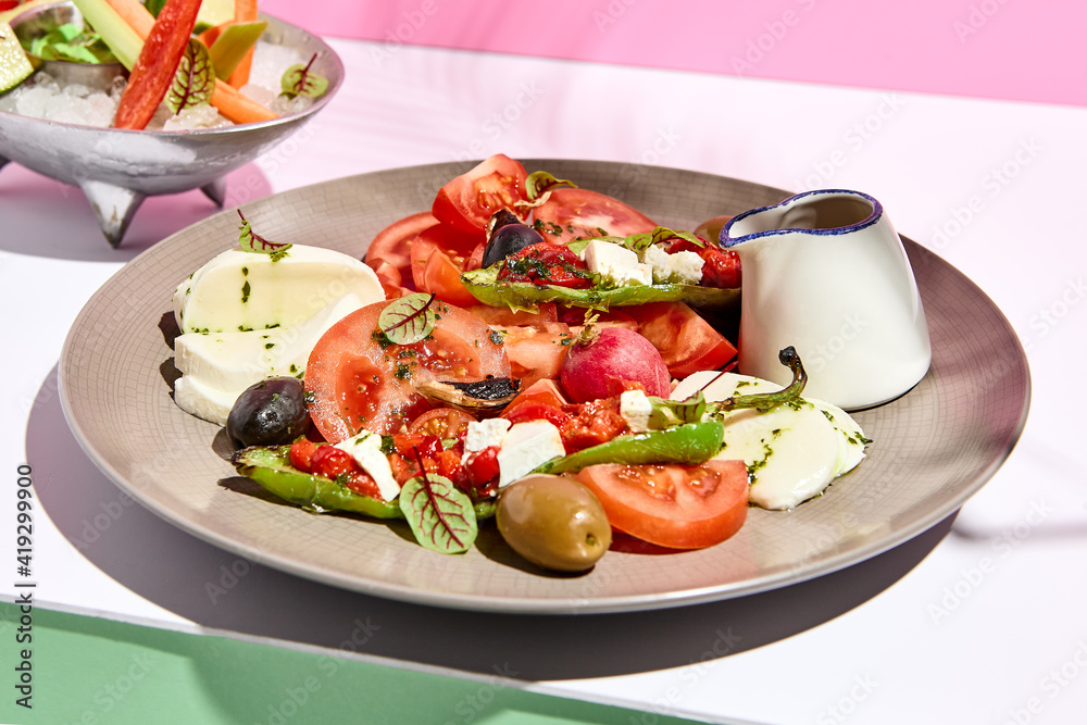 Tomato, olives and mozzarella salad . Restaurant appetizer plate on white table with pink wall. Day sunlight with hard shadow of fern palm leaves. Summer or spring restaurant food concept