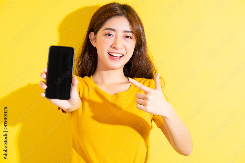 Young Asian girl uisng smartphone on yellow background Young Asian girl uisng smartphone on yellow background