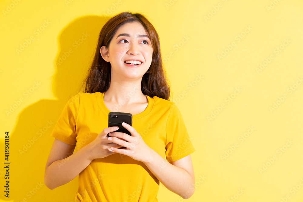 Young Asian girl uisng smartphone on yellow background