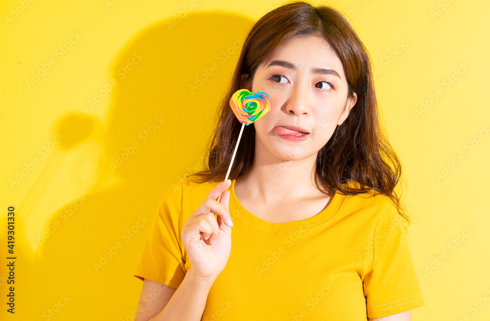 Young Asian woman eating lollipop on yellow background Young Asian woman eating lollipop on yellow background