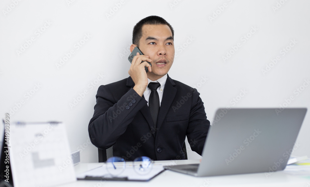 Asian man employee talking on the phone and working in a laptop with a smiling face, Office staff work and telephone conversations, Business conversation over the phone, handsome male in a black suit. Asian man employee talking on the phone and working in a laptop with a smiling face, Office staff work and telephone conversations, Business conversation over the phone, handsome male in a black suit.