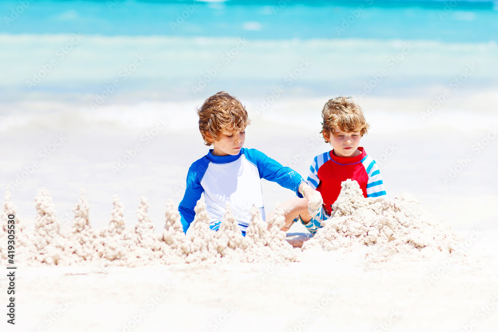 Two little kids boys having fun with building a sand castle on tropical beach. Happy children, siblings, twins and best friends playing together on their vacations