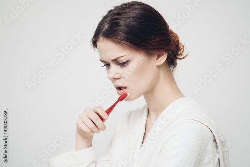 morning procedures woman brushes teeth on a light background and a white robe