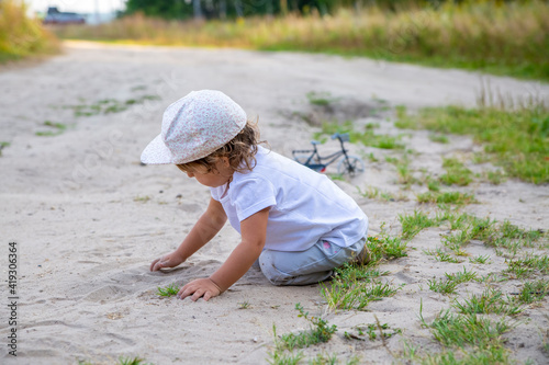 cute happy toddler in a cap crawls on all fours along a country road in the sand on a sunny summer day