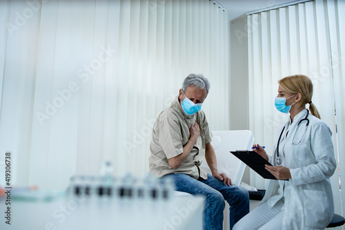 An elderly man not feeling well while doctor writing down symptoms during COVID-19 pandemic. photo