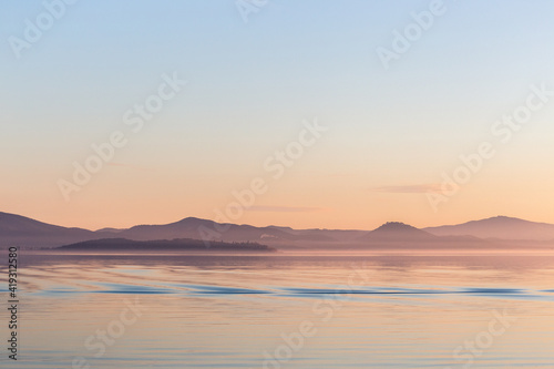 Sunset on Trasimeno lake  Umbria  Italy   with empty sky and beautiful water reflections