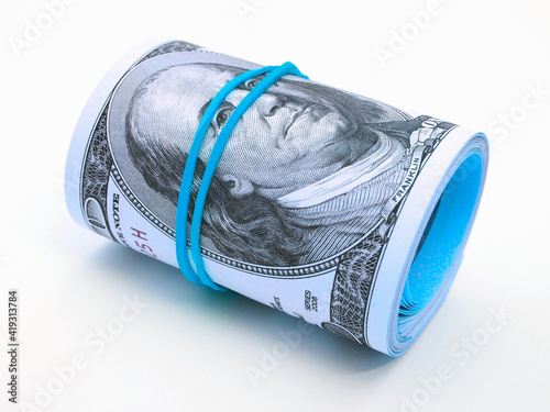 A bundle of old-style 100 hundred dollar bills lies on a white surface. Banknotes are rolled up and tied with an elastic band. Light tinted illustration on stimulating the US economy. Macro