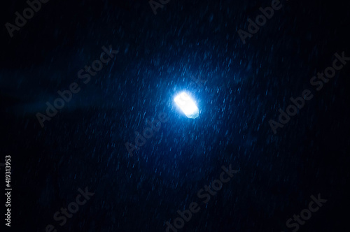 Blue street lamp at night during a snowfall on a dark background