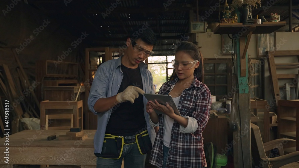 Asian carpenter or craftsman teach woman worker for wood working in workplace area and they look happy to discuss together. team are check quality the wood specification in product.