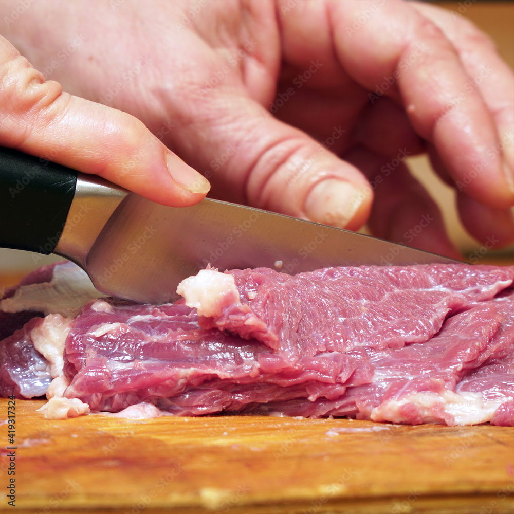 Women's hands cut meat with a kitchen knife into pieces